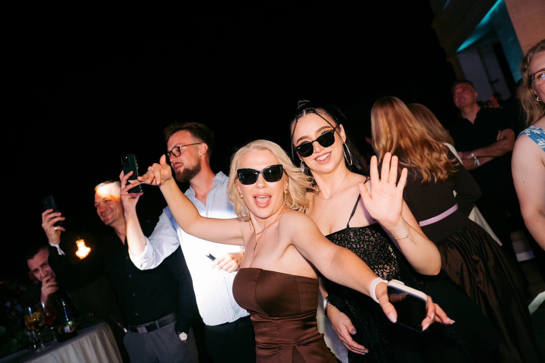 Grup de invitați sărbătorind, cu ochelari de soare, noaptea