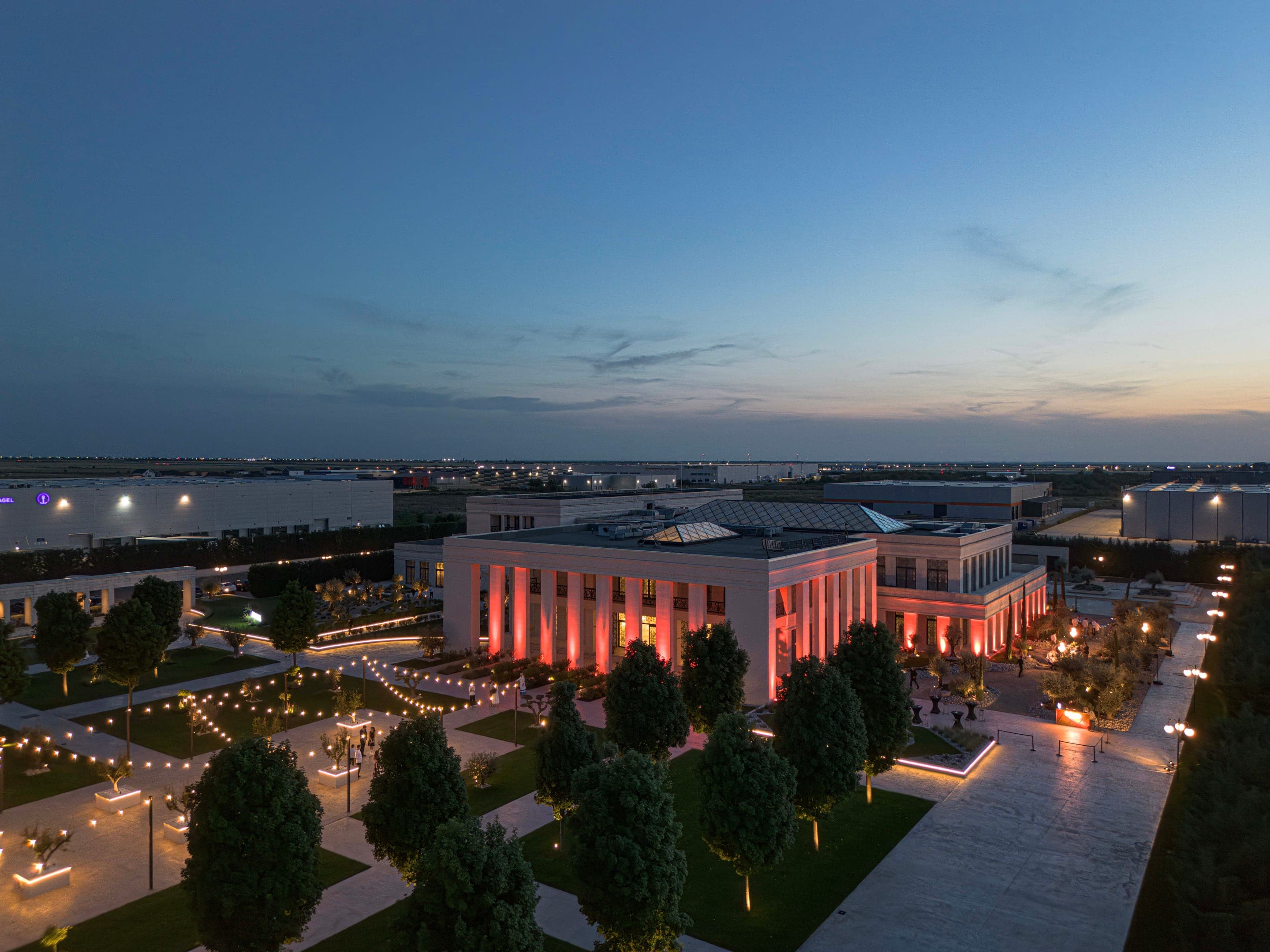Armonia Venue la asfințit, văzută de sus — clădirea luminată și grădinile cu măslini